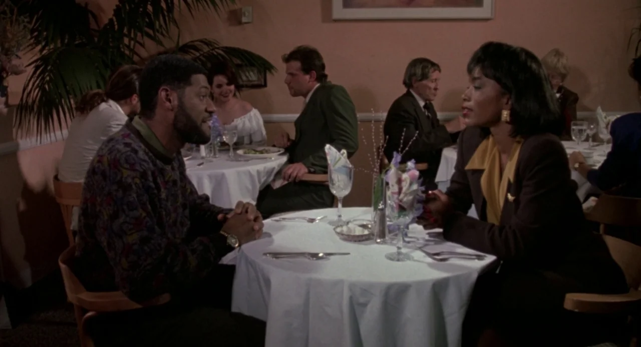 Boyz In The Hood (1991) movie still: medium — A restaurant dining room features round tables with white linens and indoor potted plants. A man and a…
