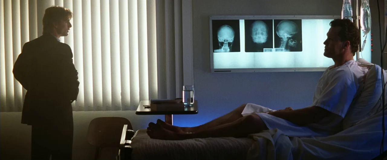 Days of Thunder (1990) movie still: medium — A medical room features a patient in a bed and a visitor standing nearby. The walls display bright…