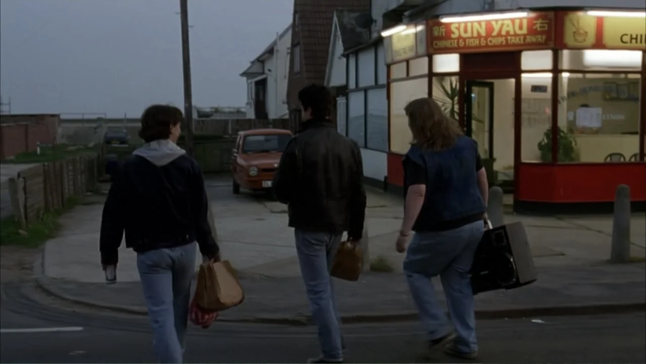 Starter for 10 (2006) movie still: fullbody — A suburban street corner at twilight features a small Chinese takeaway shop front. Three young adults…