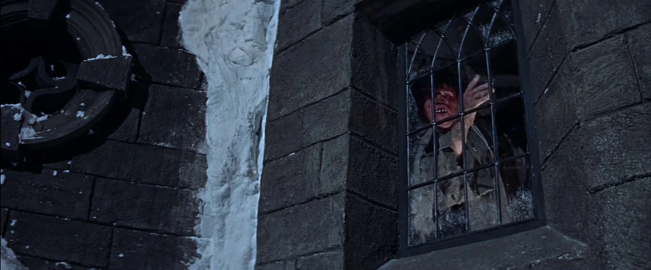 The Fearless Vampire Killers (1967) movie still: medium — A dark stone exterior wall of a building shows snow patches and a small window. A…