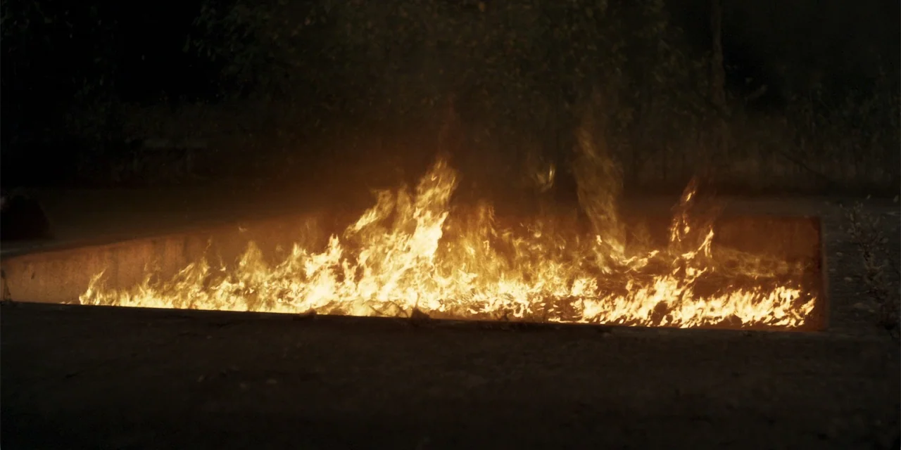 Demonic (2015) movie still: wide — A dark outdoor space contains a rectangular, sunken fire pit filled with active flames. The bright fire…