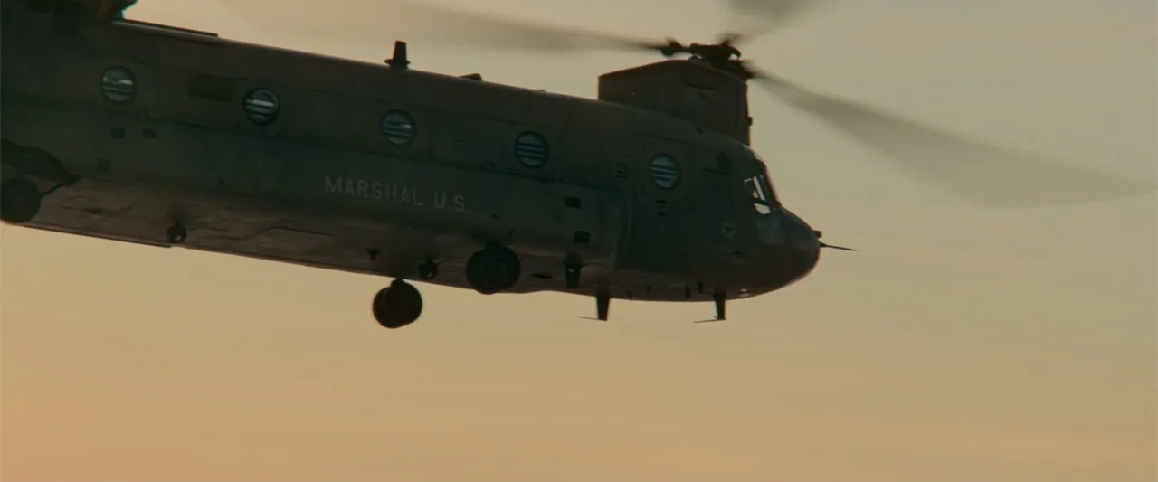 Bad Boys: Ride or Die (2024) movie still: wide — An olive drab tandem-rotor helicopter flies through an open sky at golden hour. The words MARSHAL…