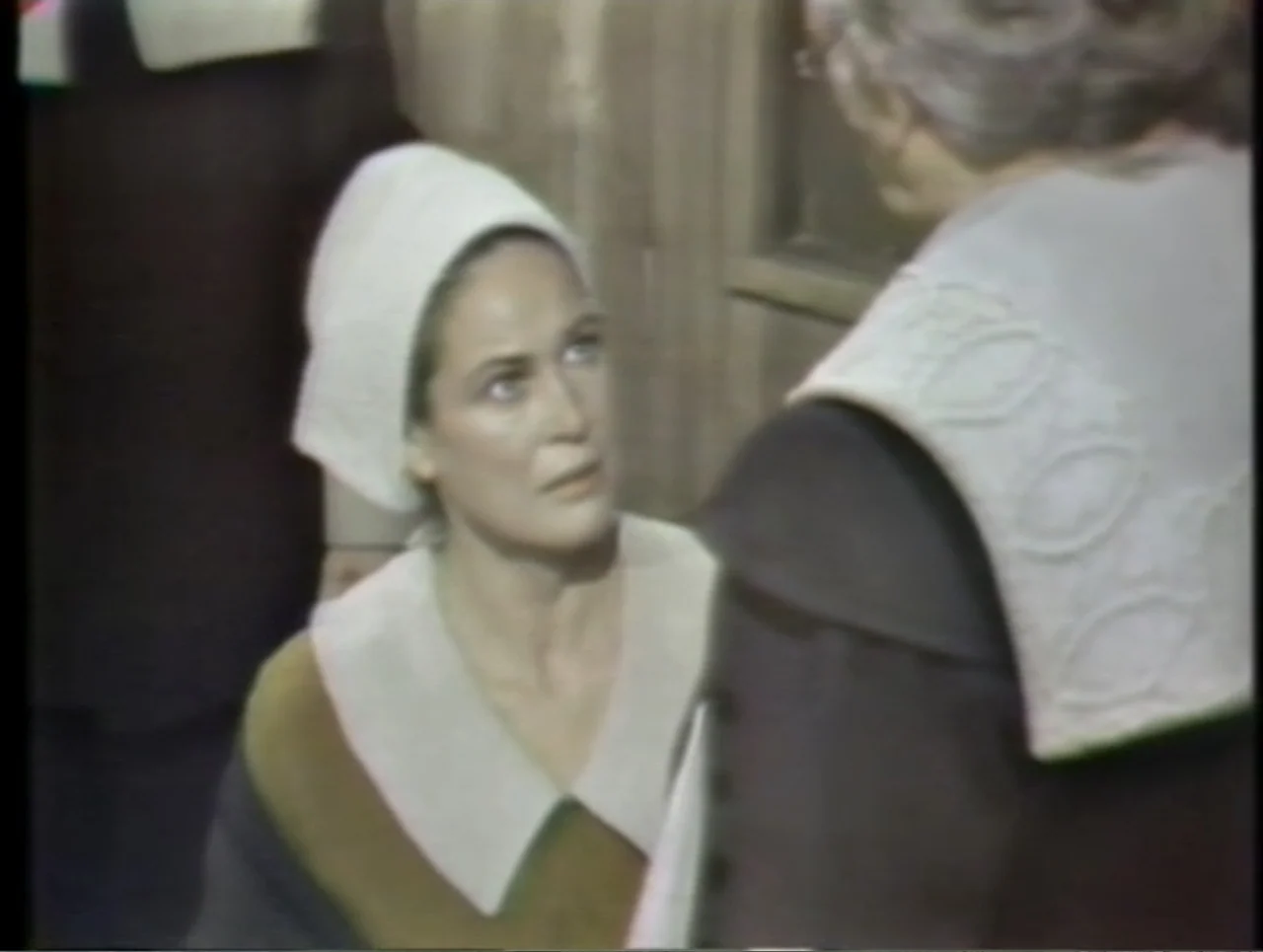 The Crucible (1996) movie still: medium — Two figures wearing white caps and collars stand inside a stone structure. A woman looks toward an older…