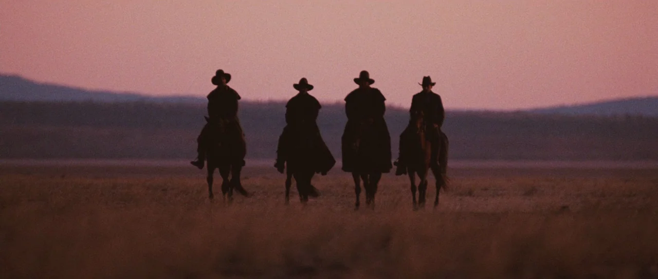 Australia (2008) movie still: wide — An expansive open desert plain under a pink-hued sunset sky. Four men on horseback ride across the landscape in…