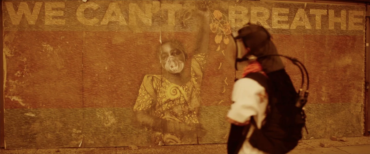 Breathe (2011) movie still: medium — A person in tactical gear and a gas mask walks along a concrete street. Behind them is a large wall mural with…