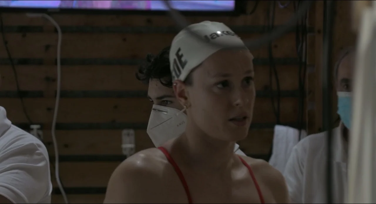 Federica Pellegrini - Underwater (2022) movie still: medium — A locker room with wooden slatted walls and people wearing protective face masks…