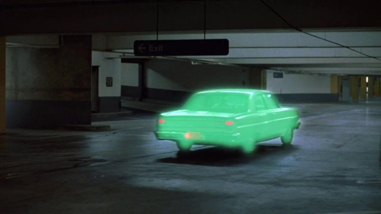 Repo Man (1984) movie still: wide — A dimly lit concrete parking garage with an exit sign hanging from the ceiling. A vintage-style sedan glows with…