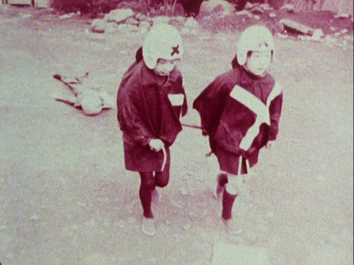Emperor Tomato Ketchup movie still: fullbody — Two children run across a flat, barren, dusty field marked by debris. Both subjects wear…