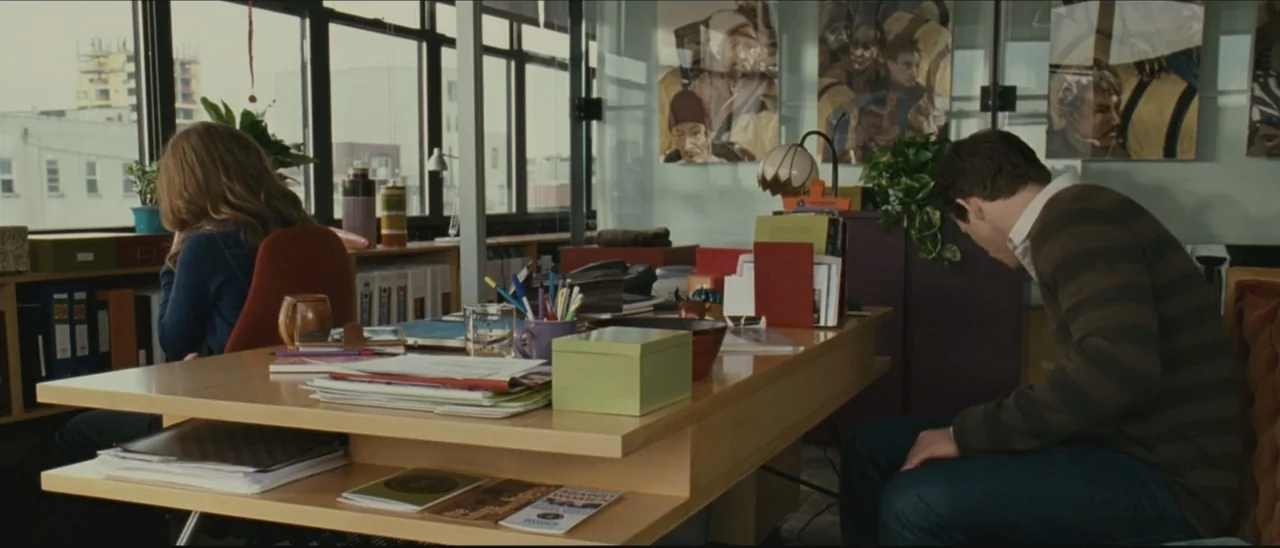 Definitely, Maybe (2008) movie still: medium — A contemporary office features a large light-wood desk littered with documents and office supplies.…