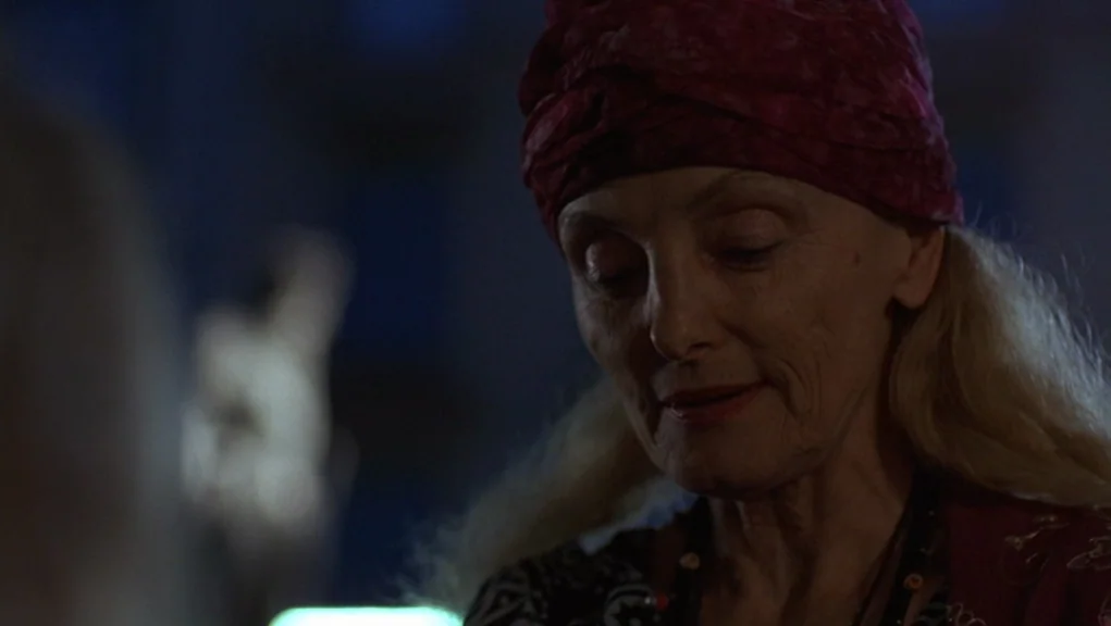Before Sunrise (1995) movie still: closeup — A dimly lit interior space with dark, indistinct shapes in the blurred background. An elderly woman in…