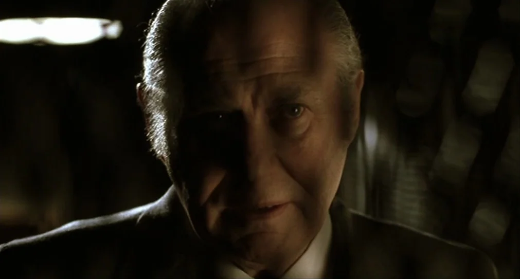 The Hurricane (1999) movie still: closeup — A dimly lit interior space features an elderly man in a formal dark suit. The subject stares ahead, half…