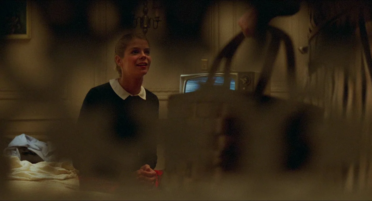 I Wanna Hold Your Hand (1978) movie still: medium — A dimly lit room features a young woman seated on the edge of a bed. She faces an individual…