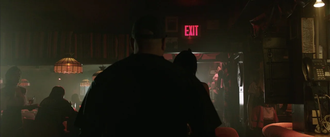 Den of Thieves (2018) movie still: medium — A dimly lit bar interior features red booth seating and pendant lights. A man stands in the foreground…