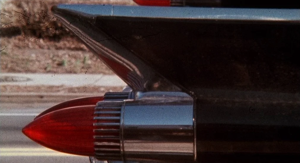 Pink Flamingos (1972) movie still: closeup — The pointed rear taillight and fin of a mid-1950s car dominate the frame. The vehicle rests on an…