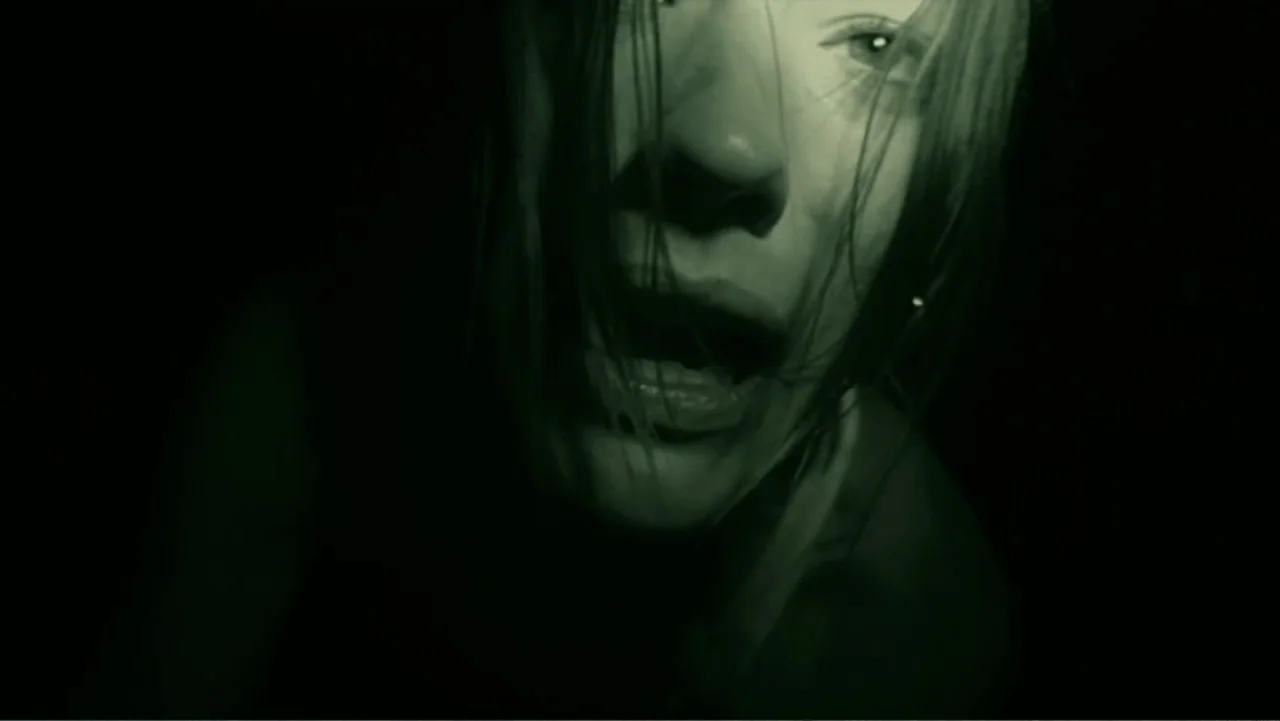 Quarantine (2008) movie still: closeup — A dark, windowless space with deep shadows hiding most architectural details. A young woman with messy hair…