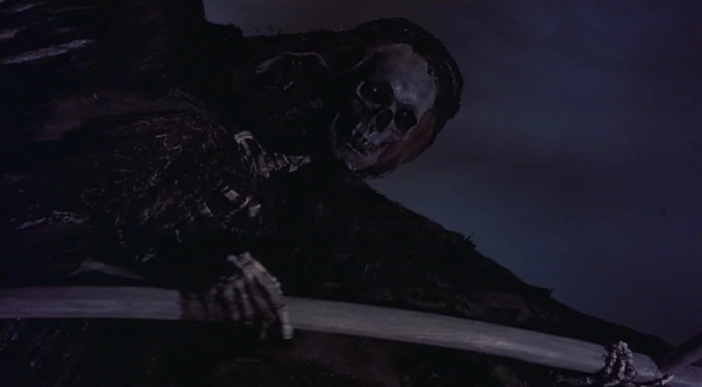 The Adventures Of Baron Munchausen (1988) movie still: closeup — A skeletal figure emerges from darkness in a dimly lit, undefined space. The figure…