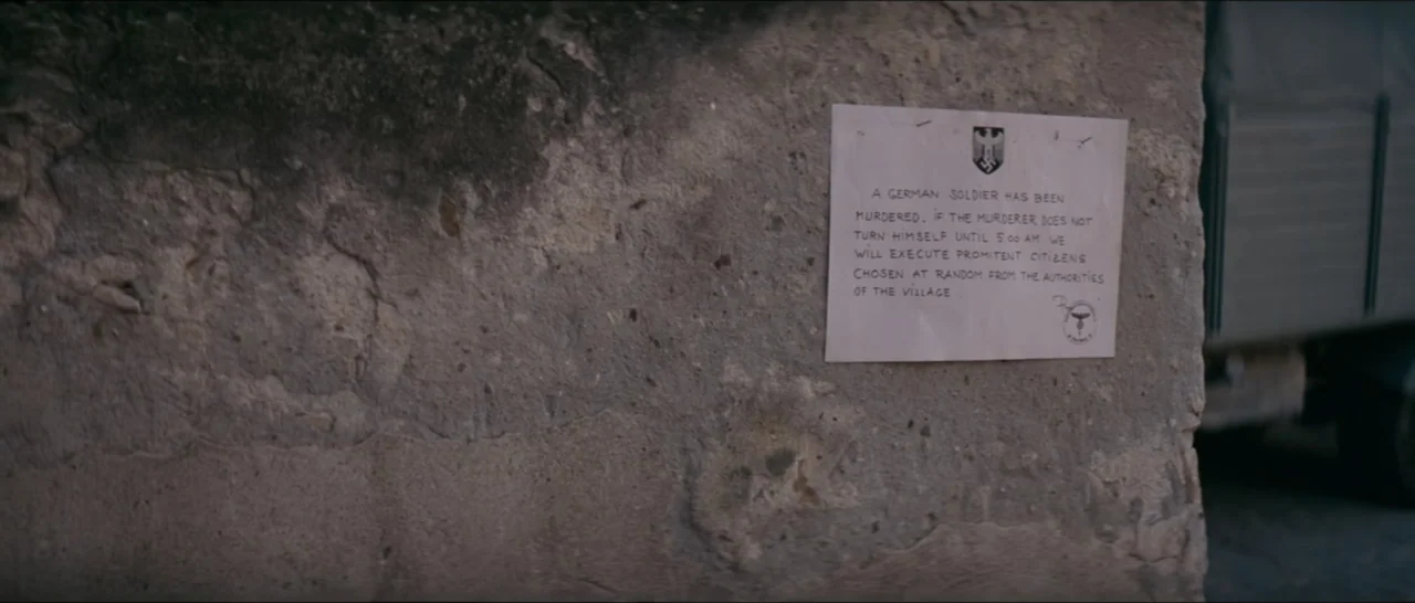 A Farewell to Fools (2013) movie still: closeup — A weathered stone wall stands in daylight with a printed paper notice adhered to it. The paper…