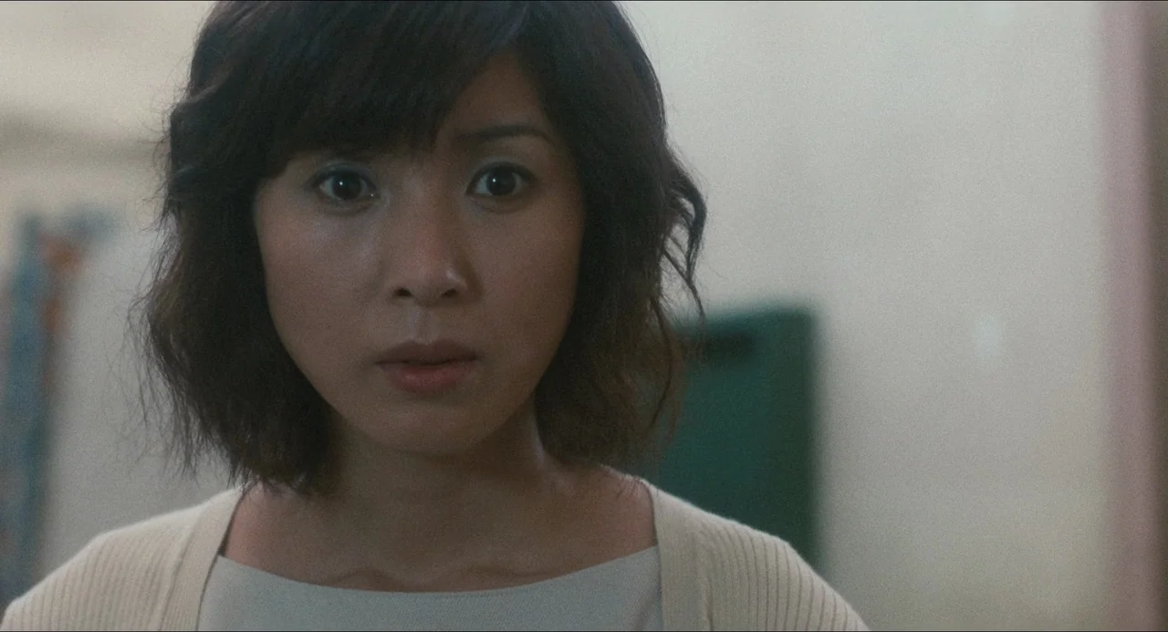 Dark Water (2002) movie still: closeup — A blurry indoor space features a wall with a dark green accent in the background. A woman with…