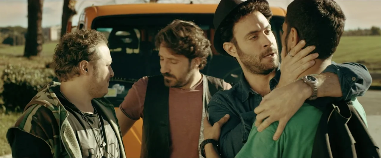 Taranta On the Road (2017) movie still: medium — A yellow van is parked outdoors in a rural landscape with distant green fields. Four men stand…