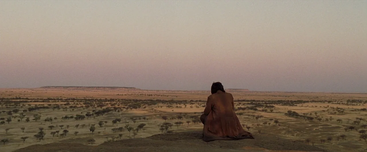 The Proposition (2005) movie still: wide — An expansive, flat arid landscape features scattered small shrubs under a wide, clear sky. A person…