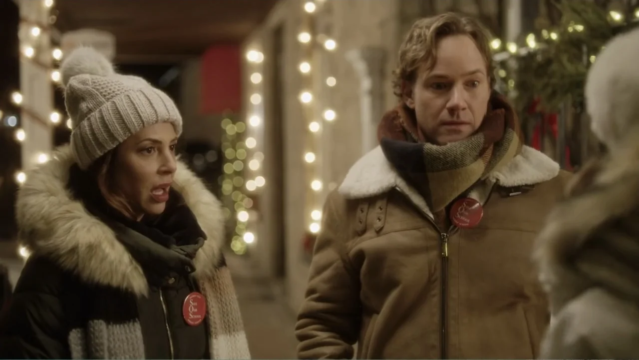 A Christmas Break (2020) movie still: medium — An outdoor evening setting features a woman and man standing on a sidewalk. The background is adorned…