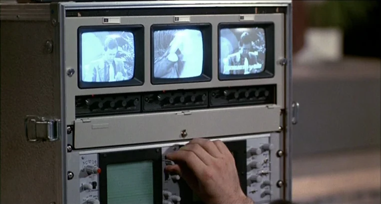 Videodrome (1983) movie still: closeup — A metal rack-mounted broadcast video console sits in a dimly lit space. A person's hand turns a dial on the…