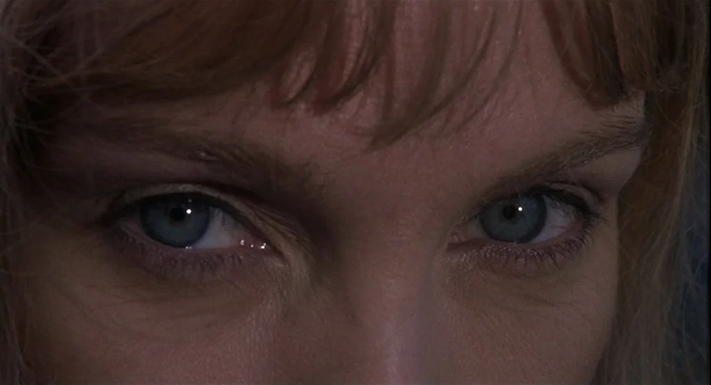 Deux (2002) movie still: closeup — A close-up view of a woman's eyes framed by her auburn bangs. The subject is looking forward, filling the entire…