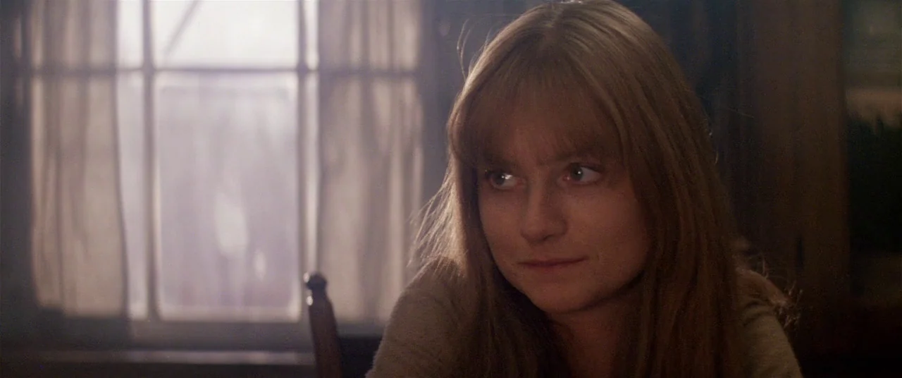 Heaven’s Gate (1980) movie still: closeup — A dimly lit room features a window with simple curtains in the background. A young woman with long hair…