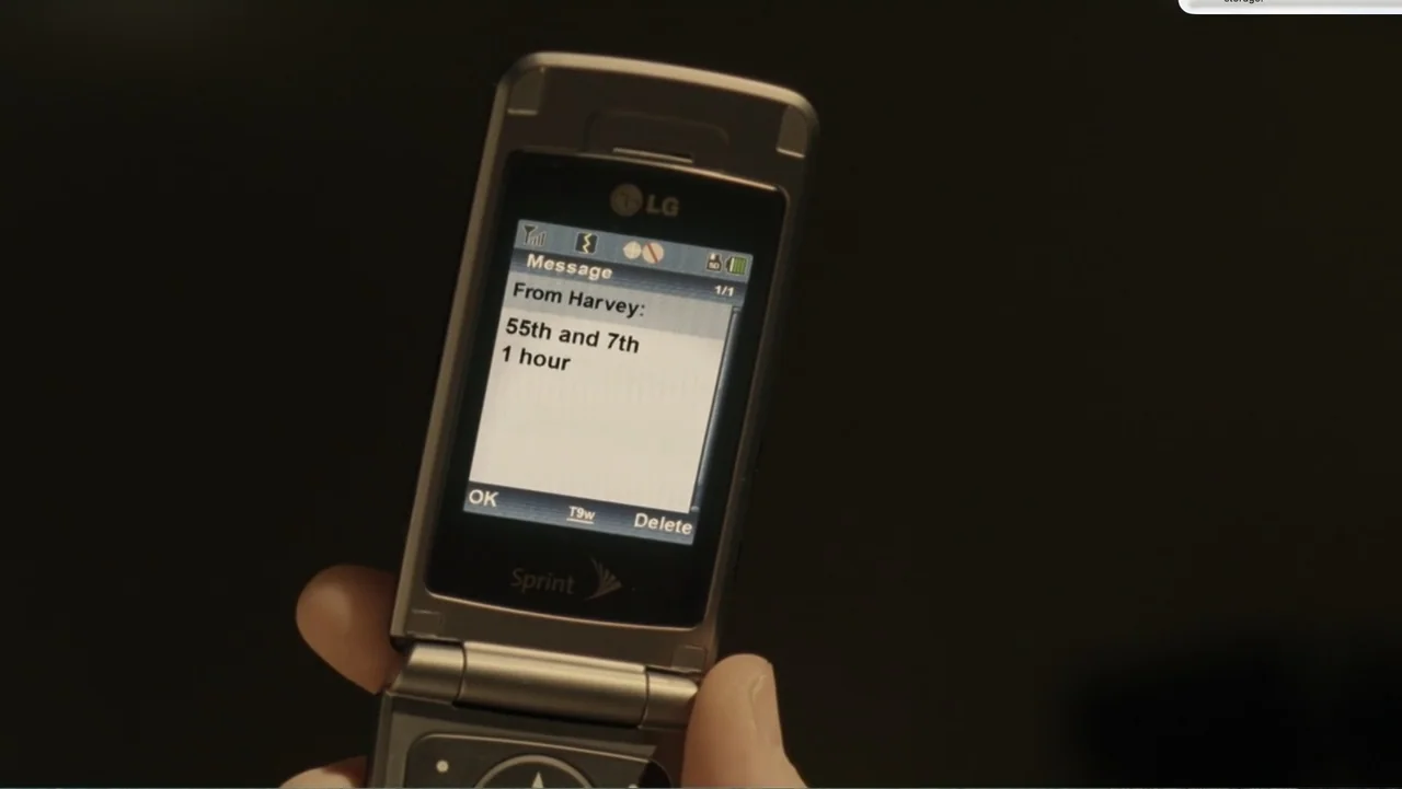 Fighting (2009) movie still: closeup — A silver LG flip phone is held in a person's hand against a dark background. The phone screen displays a text…