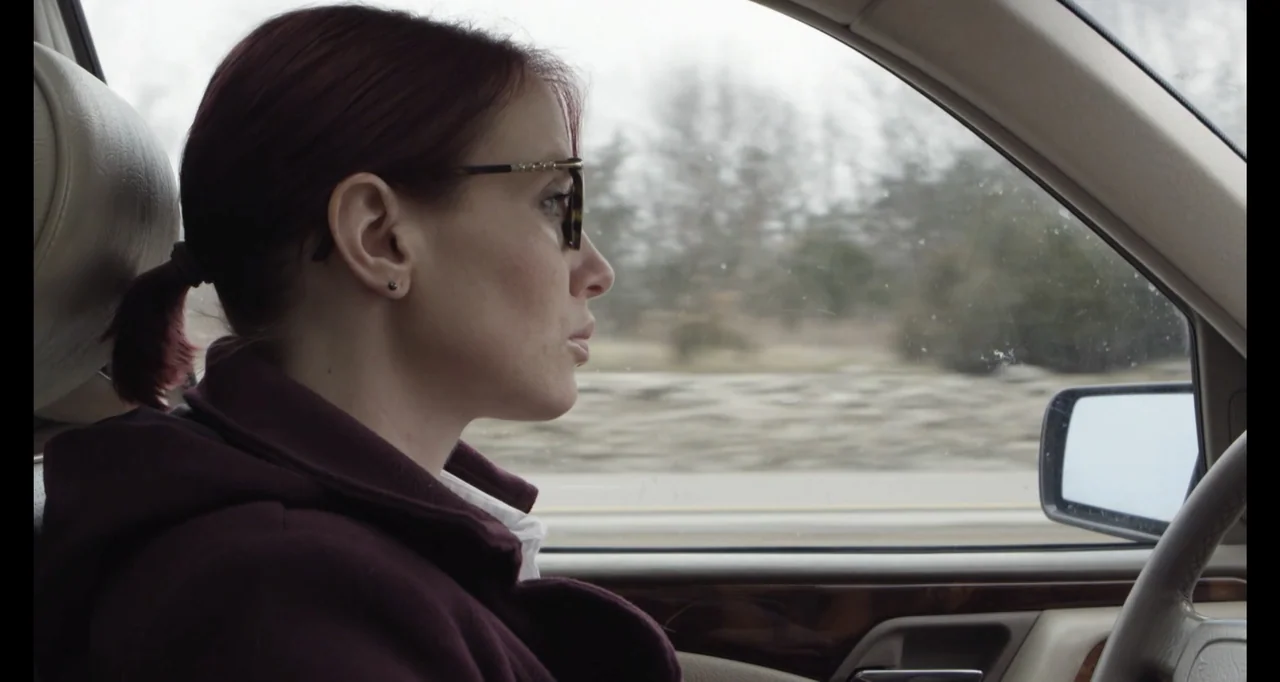 Abortion: Stories Women Tell (2016) movie still: medium — Inside a moving vehicle, a woman sits in the driver seat looking forward. The blurred…