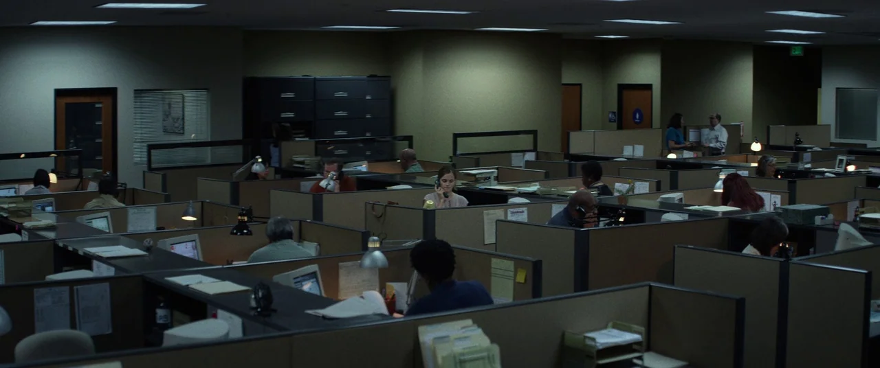 The Circle (2017) movie still: wide — A sprawling office interior features rows of tan cubicles under recessed fluorescent ceiling panels. Several…