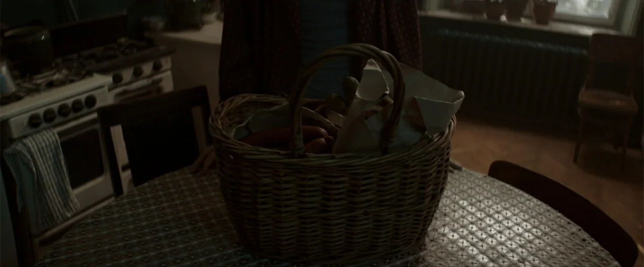 La herencia (2010) movie still: medium — A dimly lit room features a worn table with a textured plastic tablecloth. A person stands behind a large…