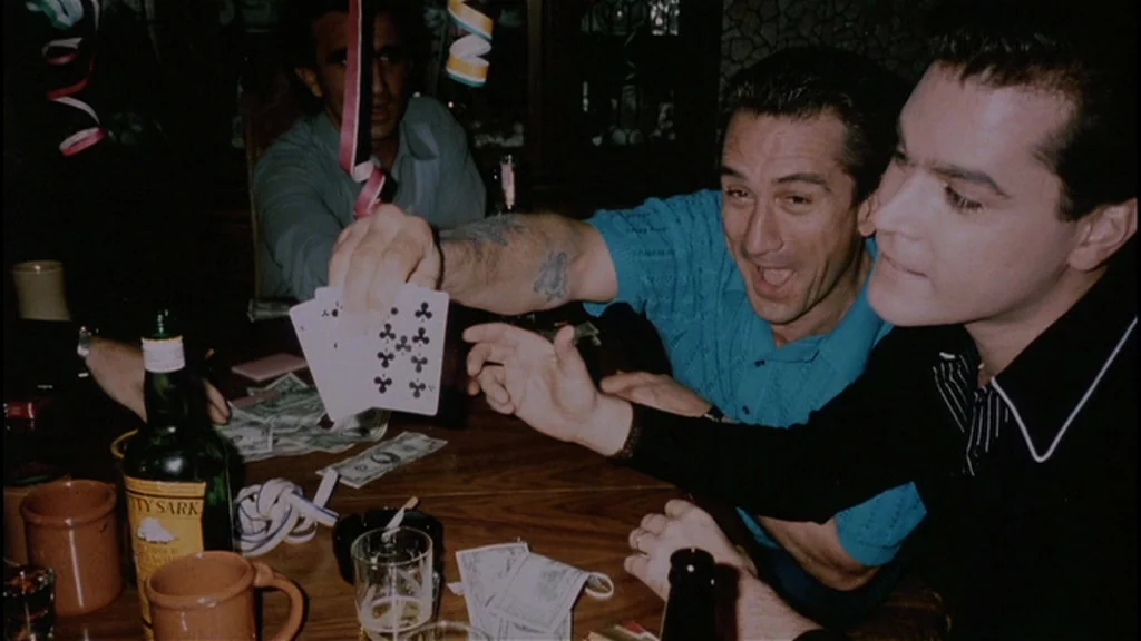 Goodfellas (1990) movie still: medium — A dimly lit room with a wooden table cluttered with paper money and bottles. Two men sit close together, one…