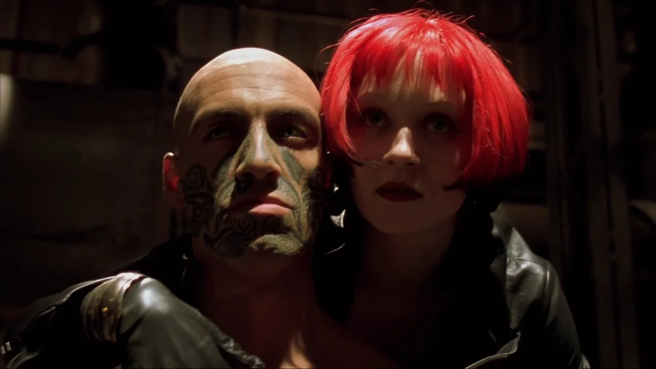 Blade II (2002) movie still: closeup — A dark, dimly lit environment features a bald man and a red-haired woman. The man has extensive facial…