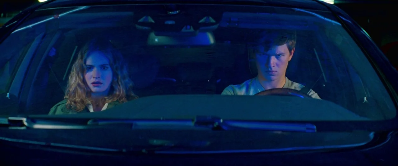 Baby Driver (2017) movie still: medium — The front interior of a car at night is filled with artificial blue light. A young man drives while a woman…