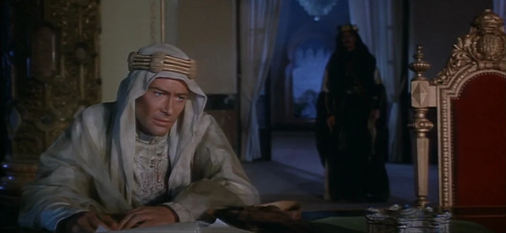 Lawrence Of Arabia movie still: medium — A dark, ornately furnished chamber features gilded architectural details and heavy drapery. A man in…