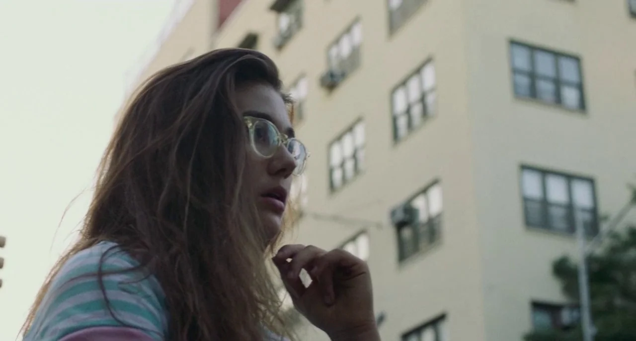 Skate Kitchen (2018) movie still: medium — An urban setting features a light-colored multi-story apartment building with several window units. A…