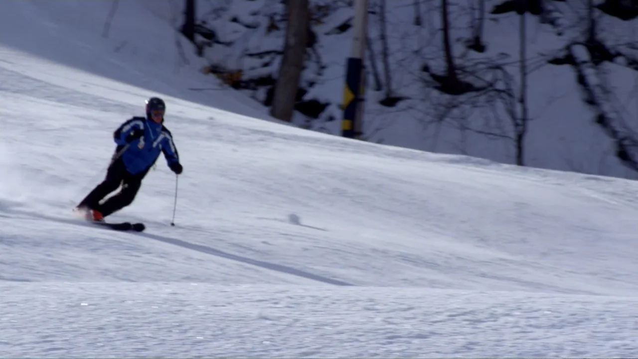 Christmas with a Prince (2018) movie still: fullbody — A steep snow-covered mountainside features bare trees at the top of the slope. A single skier…