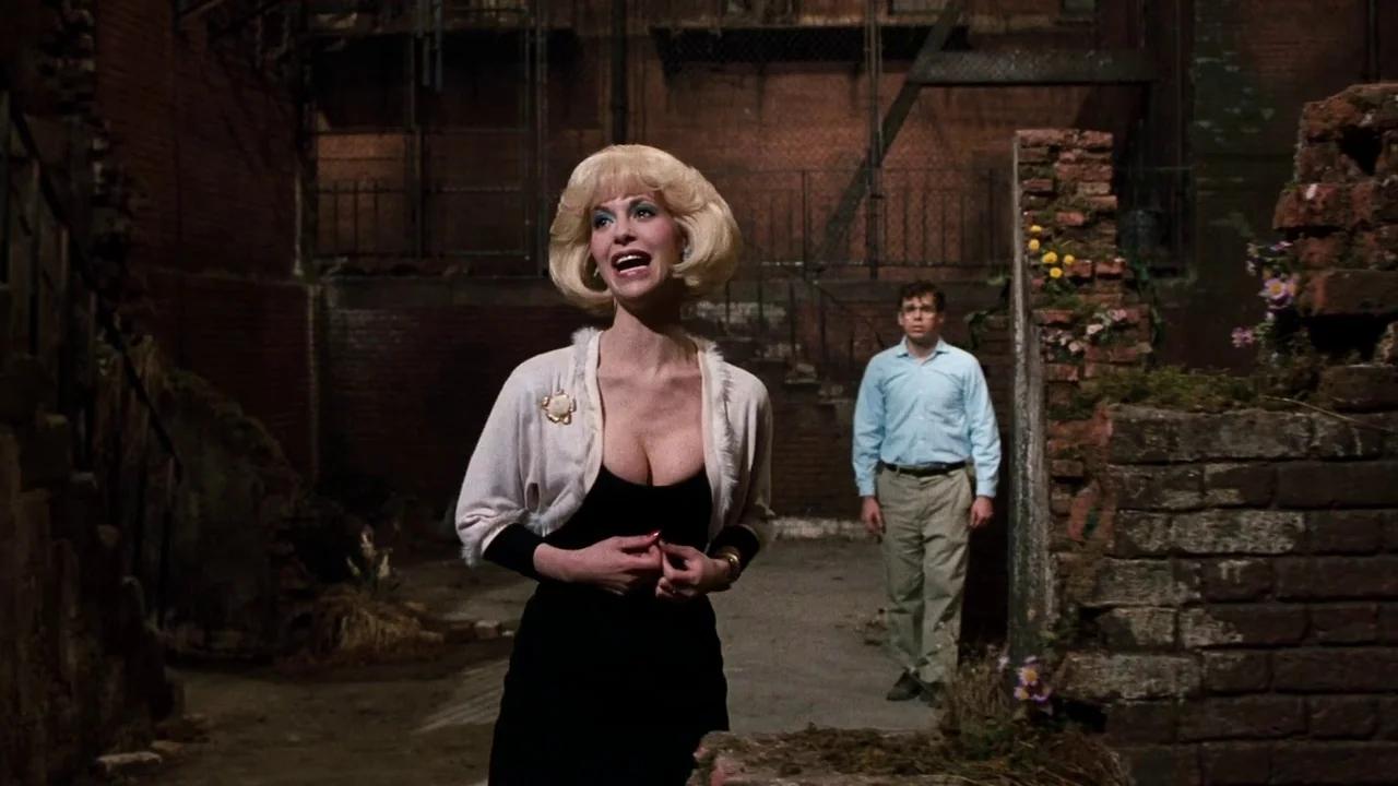 Little Shop of Horrors (1986) movie still: medium — A dimly lit brick alleyway features scattered debris and small patches of greenery. A blonde…