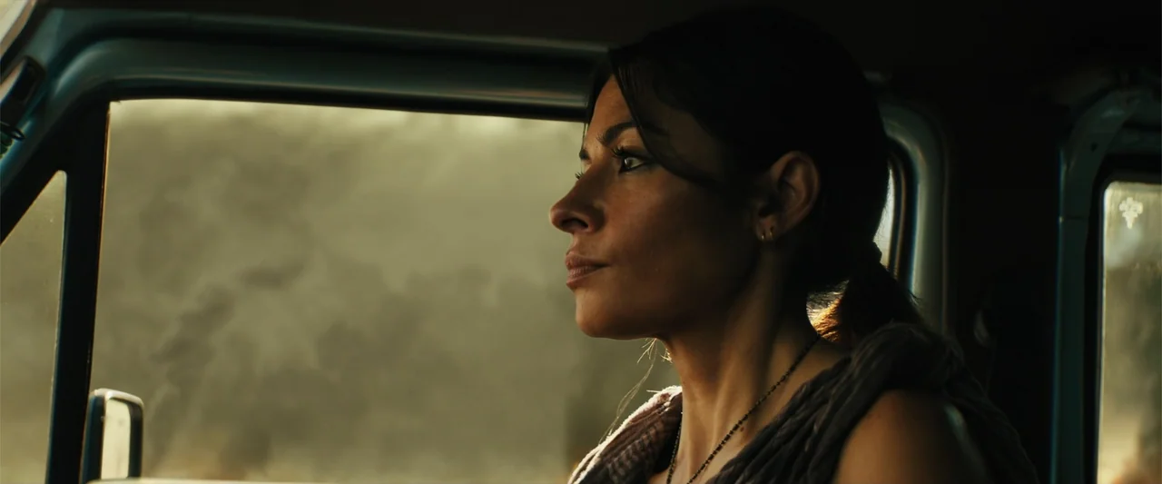 Black Adam (2022) movie still: medium — The interior of a vehicle cabin bathed in golden afternoon light through the window. A woman with dark hair…