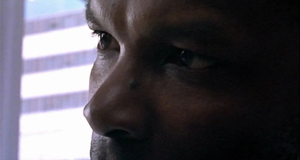 Trouble Every Day (2001) movie still: closeup — A close-up view of a man inside near a bright window looking out. The man stares across the frame…