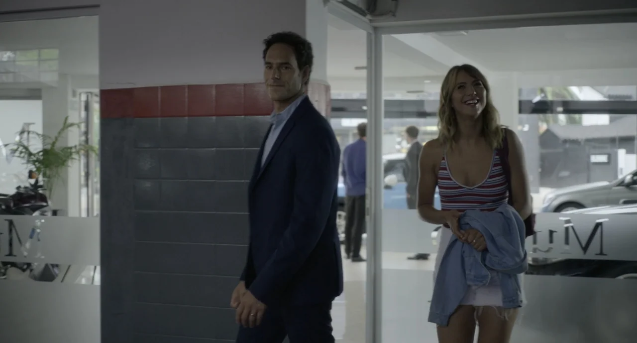 Little White Lies (2010) movie still: fullbody — A glass-fronted commercial space features gray tiled walls and reflective interior doors. A man in…
