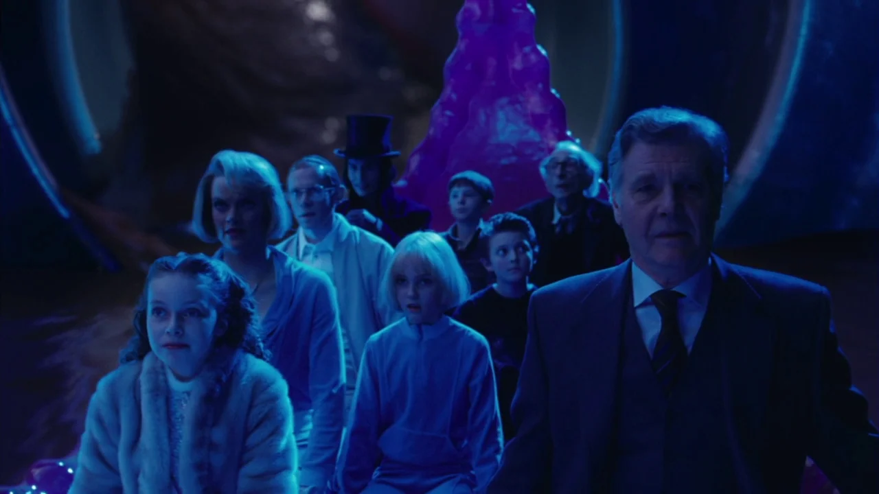 Charlie and The Chocolate Factory (2005) movie still: medium — A group of people sit on a boat moving through a dark neon-lit tunnel. Various adults…