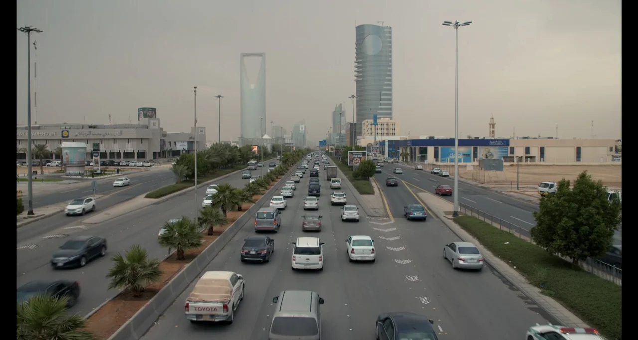 Saudi Women's Driving School (2019) movie still: establishing — A wide view of a multi-lane urban highway with heavy traffic in a city. Tall modern…