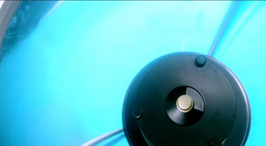 Gray’s Anatomy (1996) movie still: closeup — A close-up view looks down at the base of a modern tanning bed. The black circular headrest rests…