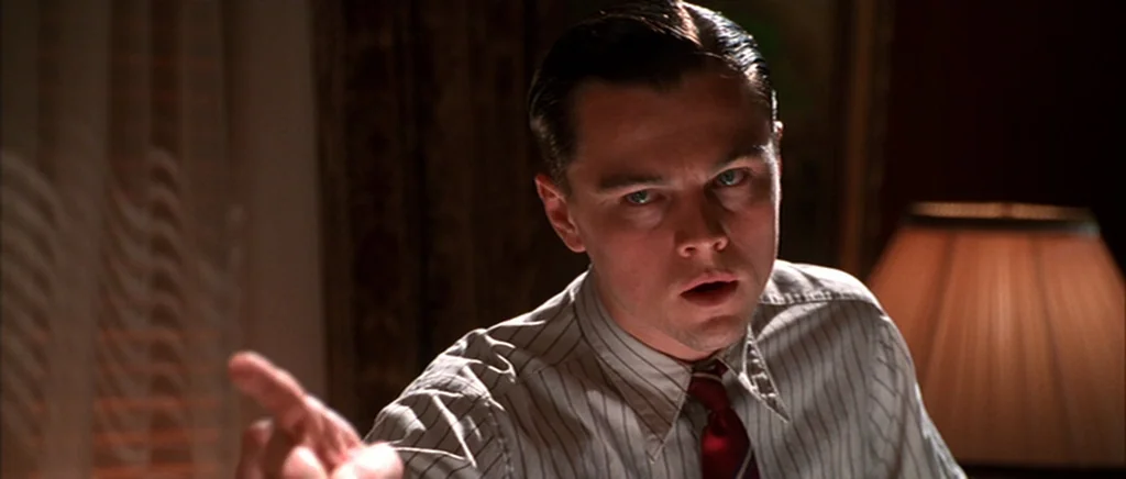 The Aviator (2004) movie still: closeup — A dimly lit room features a period-specific office setting with warm ambient light. A man in a pinstriped…