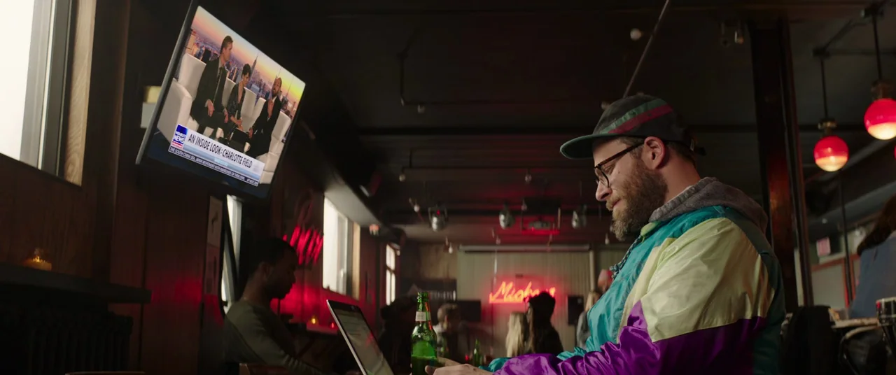 Long Shot (2019) movie still: medium — A dimly lit bar interior features red neon signs and industrial ceiling fixtures. A man sits at the bar,…