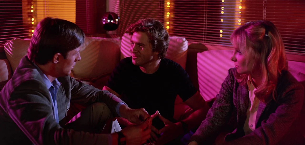 Tron (1982) movie still: medium — A dark lounge environment features horizontal blinds lit by intense pink neon light. Three people sit on a plush…