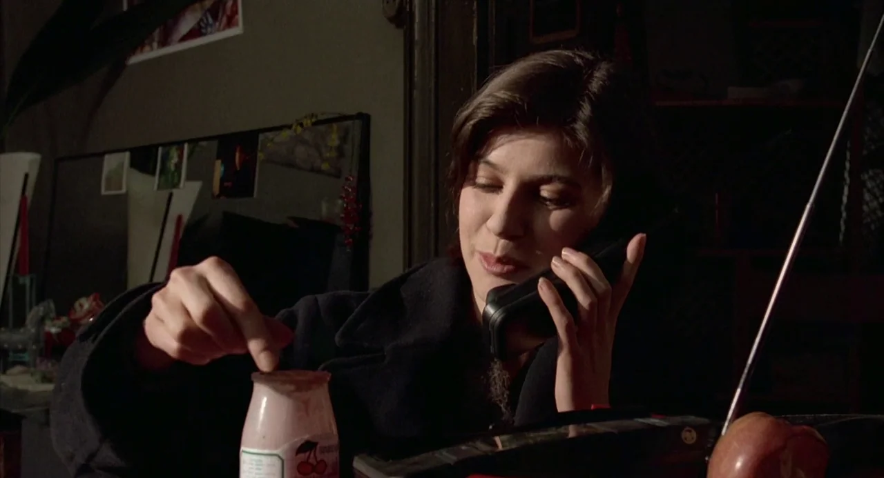 Three Colours: Red (1994) movie still: medium — A dimly lit room with dark walls and scattered personal items in the background. A woman sits in the…