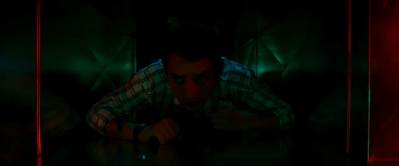 Cooties (2014) movie still: medium — A dark, cramped metallic air duct glows with sharp red and green side lighting. A man in a plaid shirt crawls…